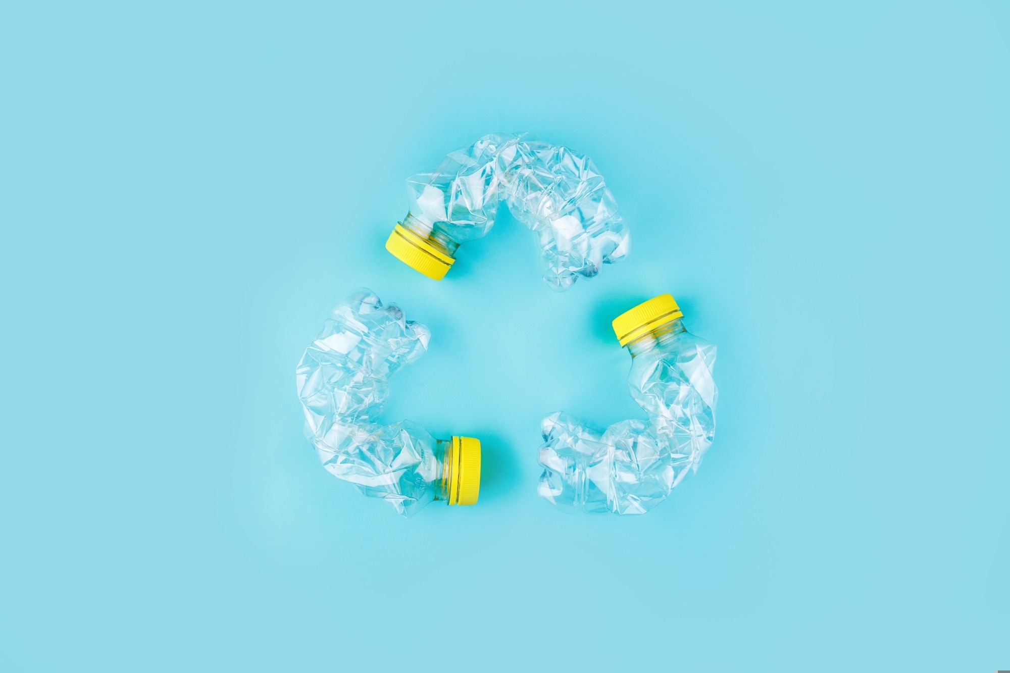 Three crashed plastic bottles on blue background form resycling sign.
