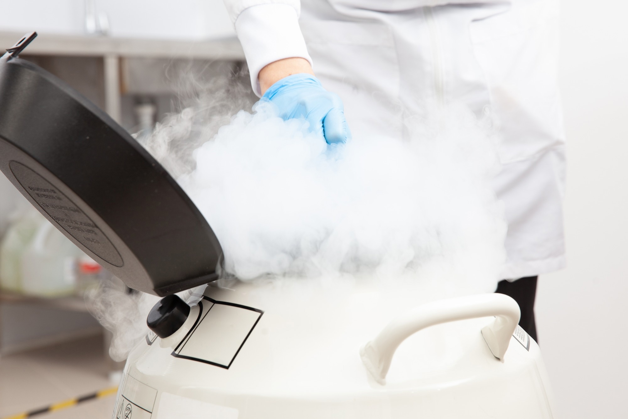 A researcher in a lab coat handling a cryogenic container with liquid nitrogen vapor, illustrating low-temperature conditions required for superconducting energy storage systems.