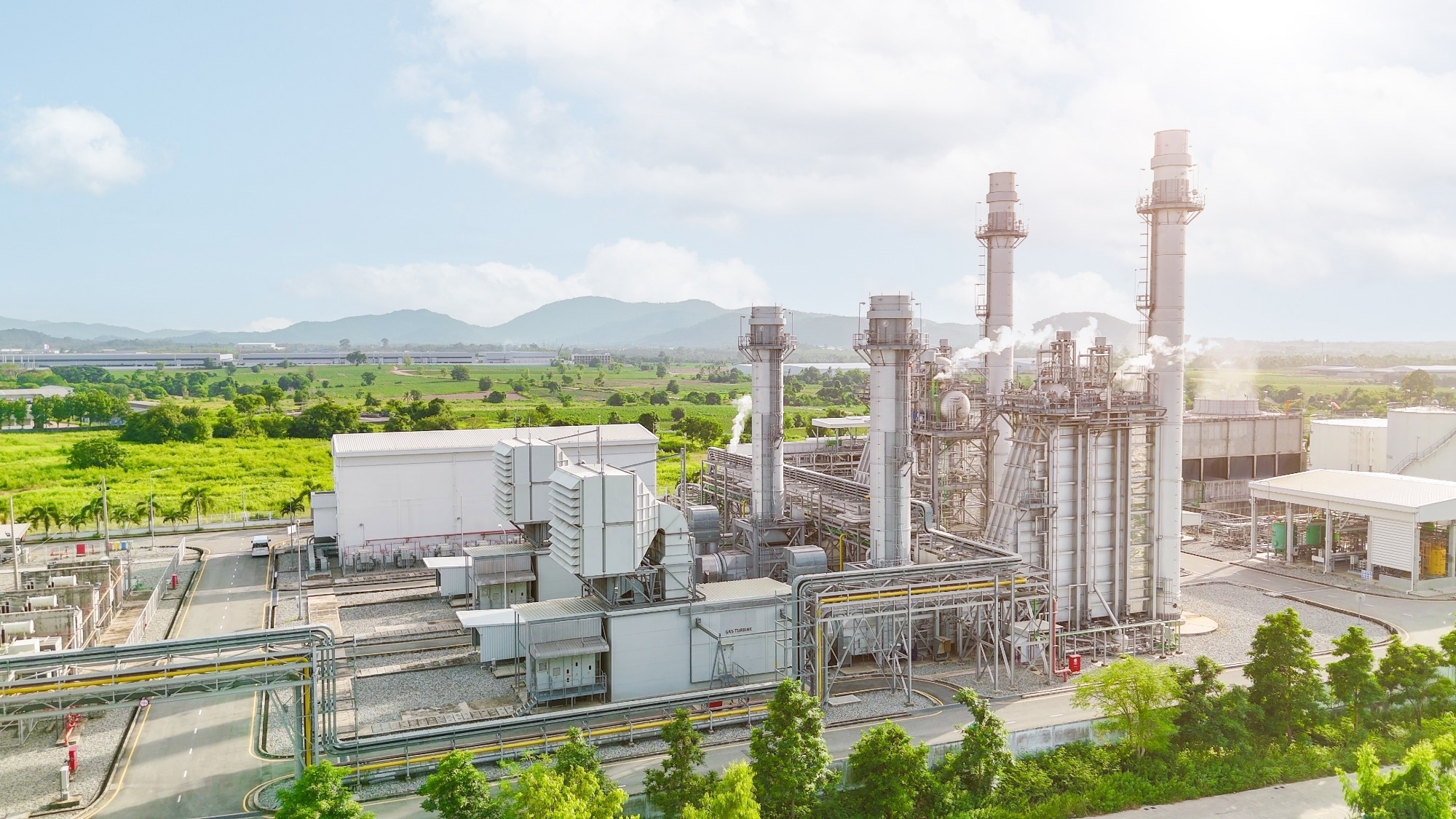 Modern industrial plant with multiple smokestacks and clean infrastructure, set against a green landscape and blue sky
