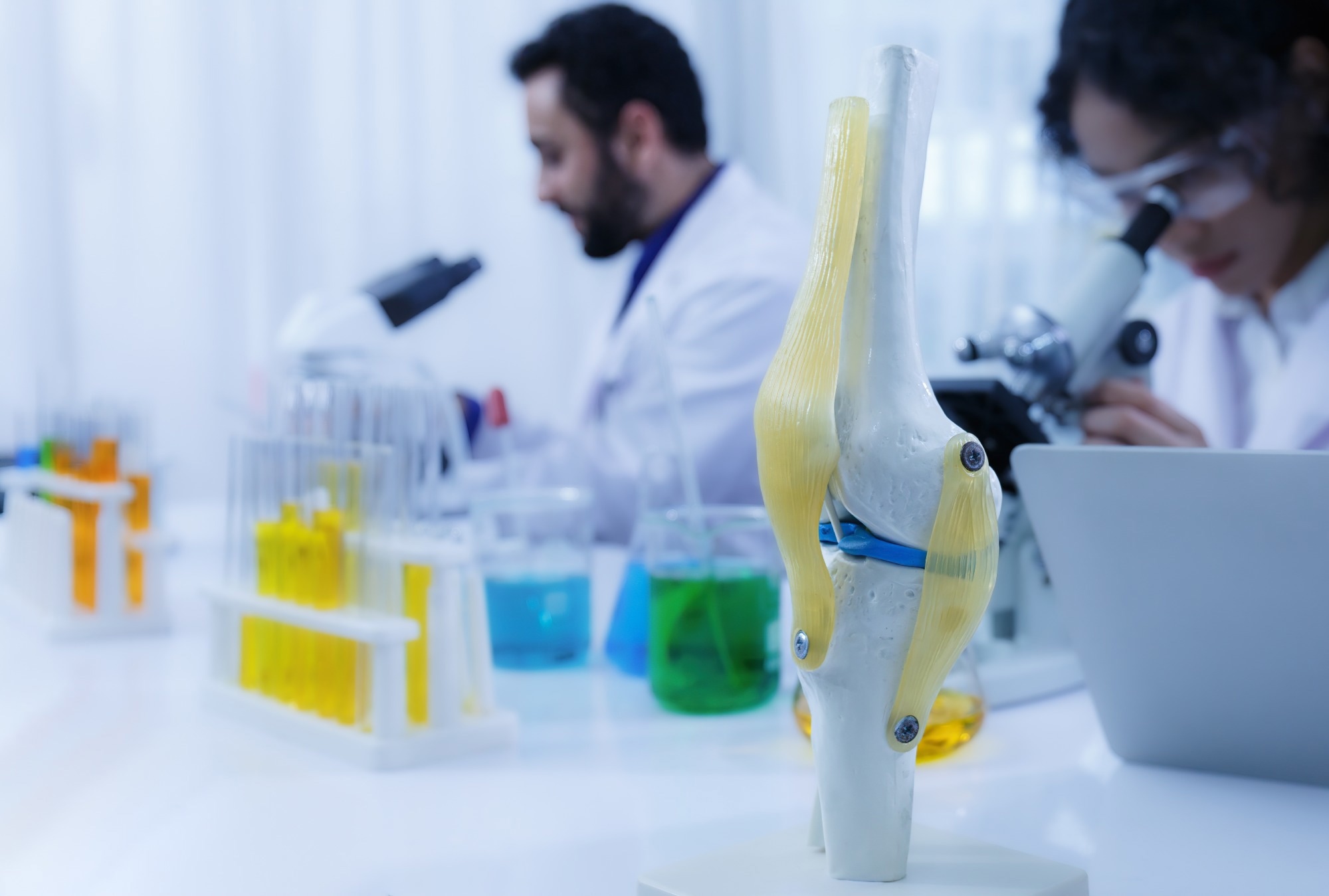 Two scientists wear white robes and protective goggles microscopes in a lab