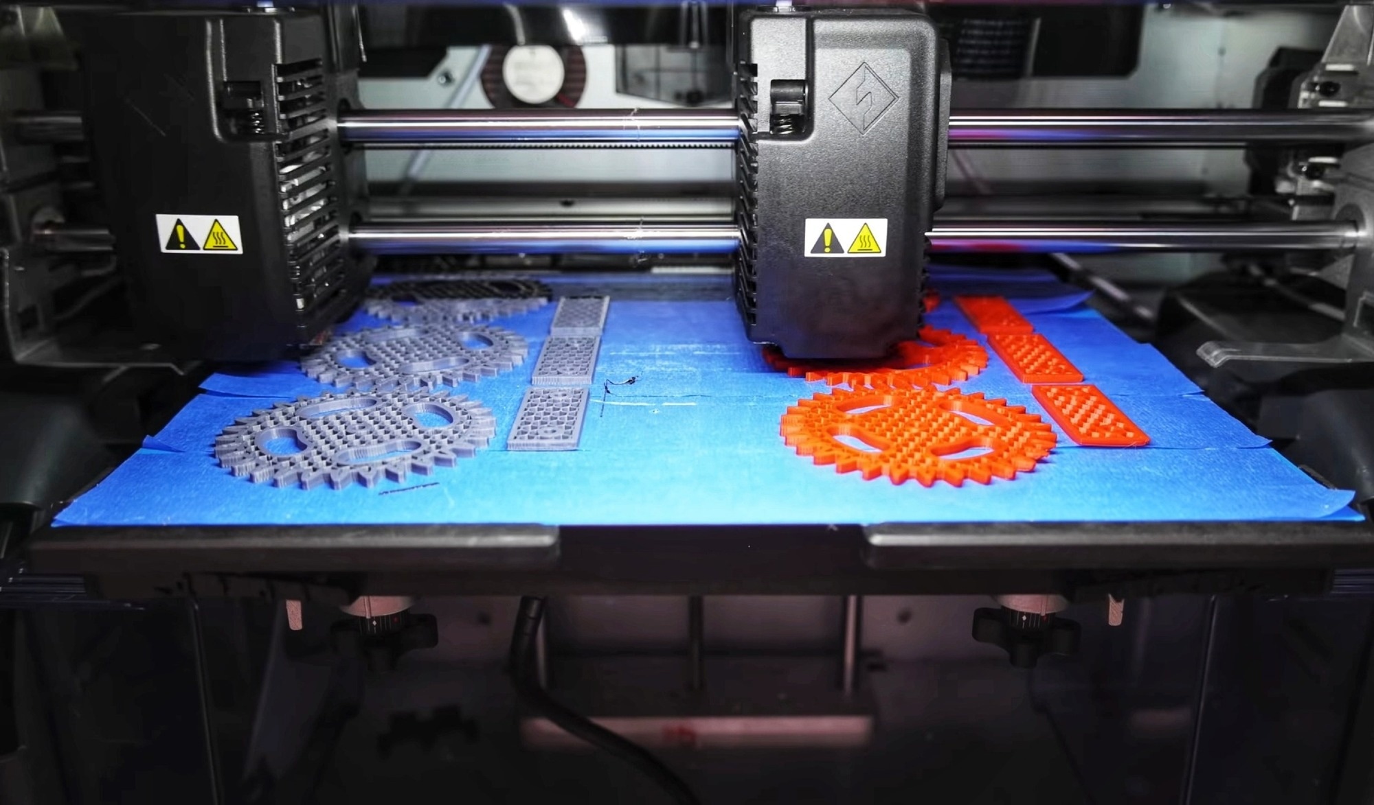3D printed machinery parts in grey and orange atop a blue surface.