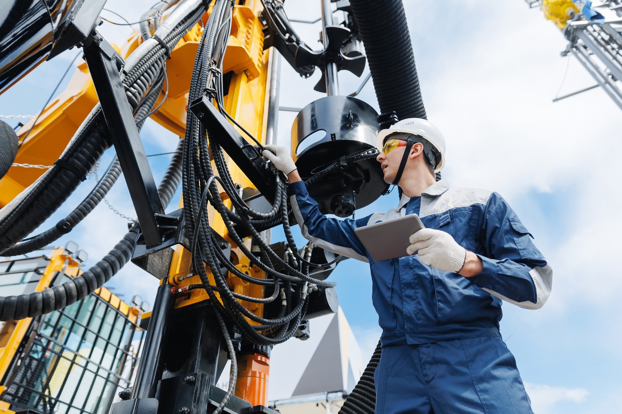 Oil and gas engineer in a blue boiler suit and white hard hat checking on systems.