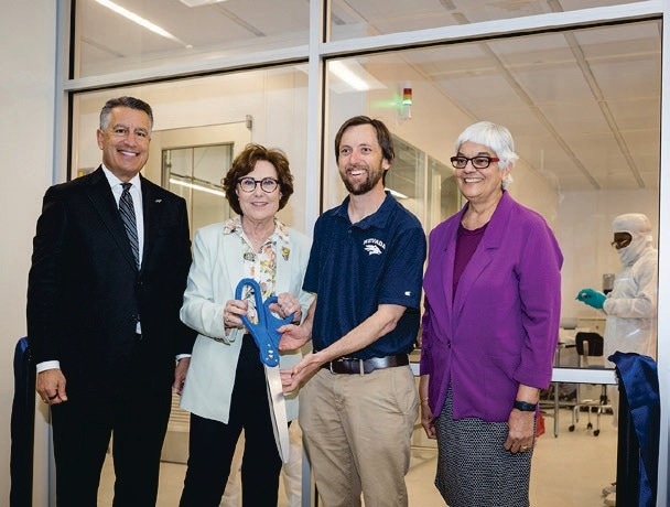 A group of people stand around Dr. Renzas holding ceremonial scissors.