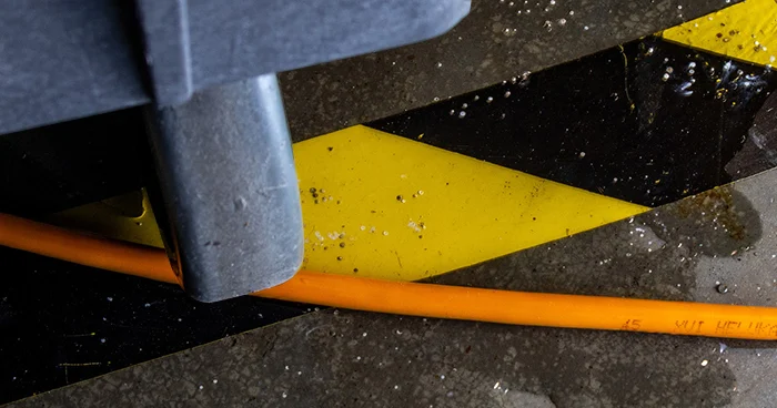An image of a cable on a work room floor with a wheel rolling over it.