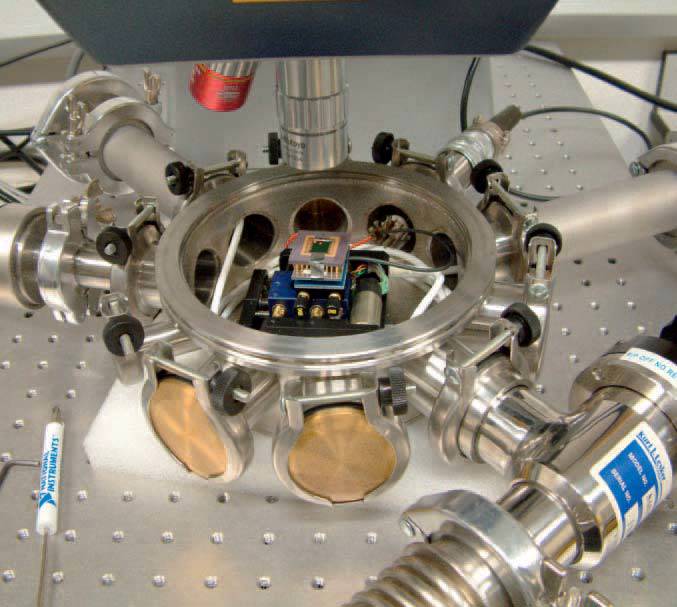 Photograph of the environmental chamber, showing a sample attached to the vacuum-compatible XY stages. The long-focal length lens can be seen above the sample, which is attached to the Polytec Micro Systems Analyzer Differential Vibrometer