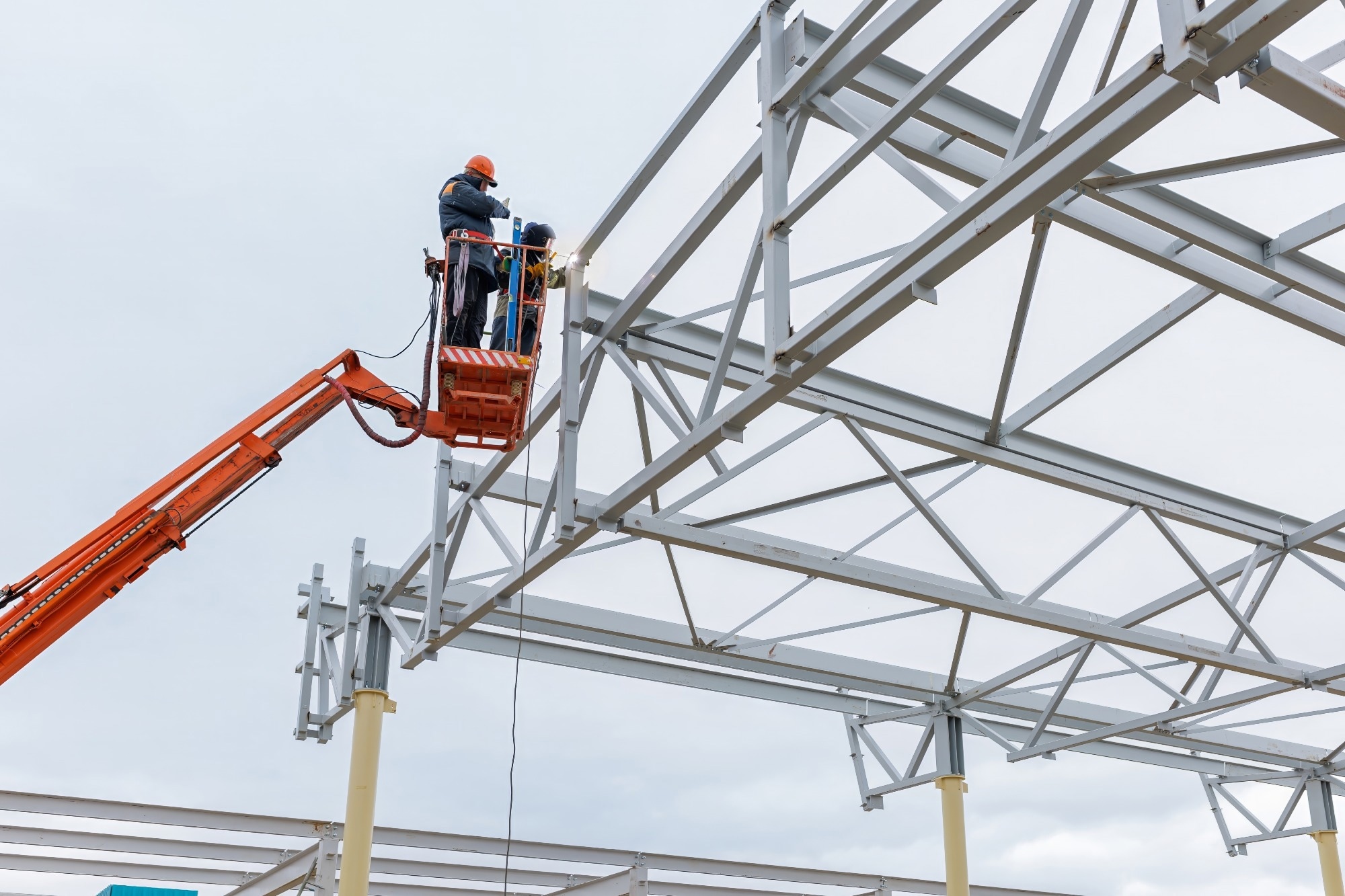 A worker on a crane performs high-rise work on welding metal structures of new tower at height