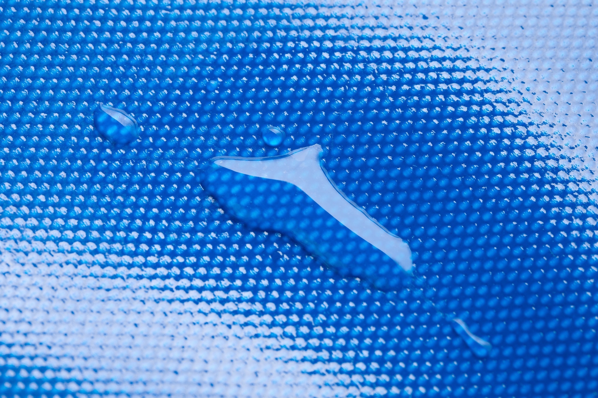 A close-up of a waterproof polymer coating with water droplets on its textured blue surface, highlighting its hydrophobic properties and durability for protective applications.