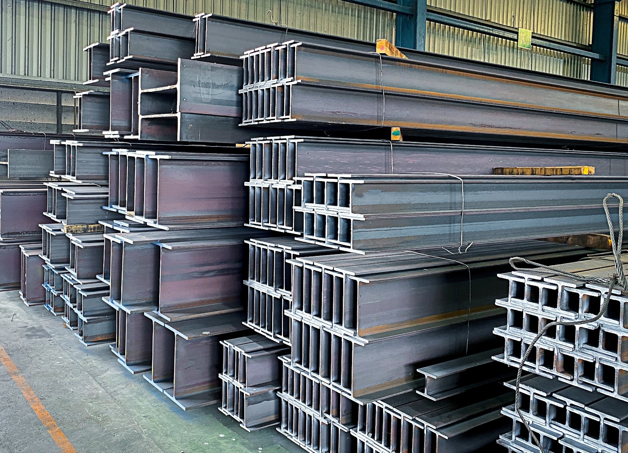 A pile of steel beams for industrial construction use are stacked in a warehouse.