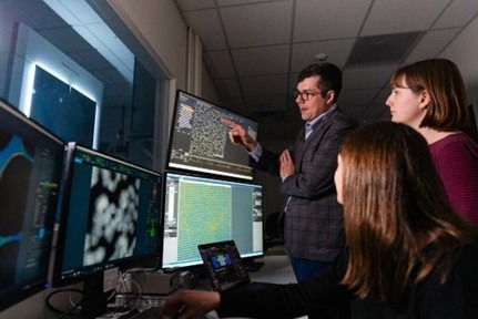 Two female and one male scientists looking at multiple PC screens in a lab
