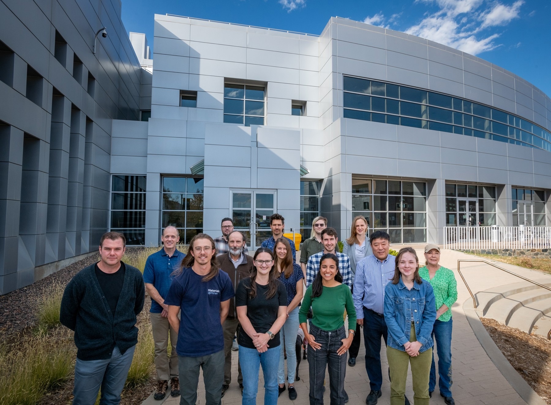 A group of scientists stood outside a large building, all smiling at the camera.