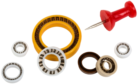 A collection of Omniseal® Spring-Energized Miniature Seals in different sizes and colors, with a pushpin for scale reference