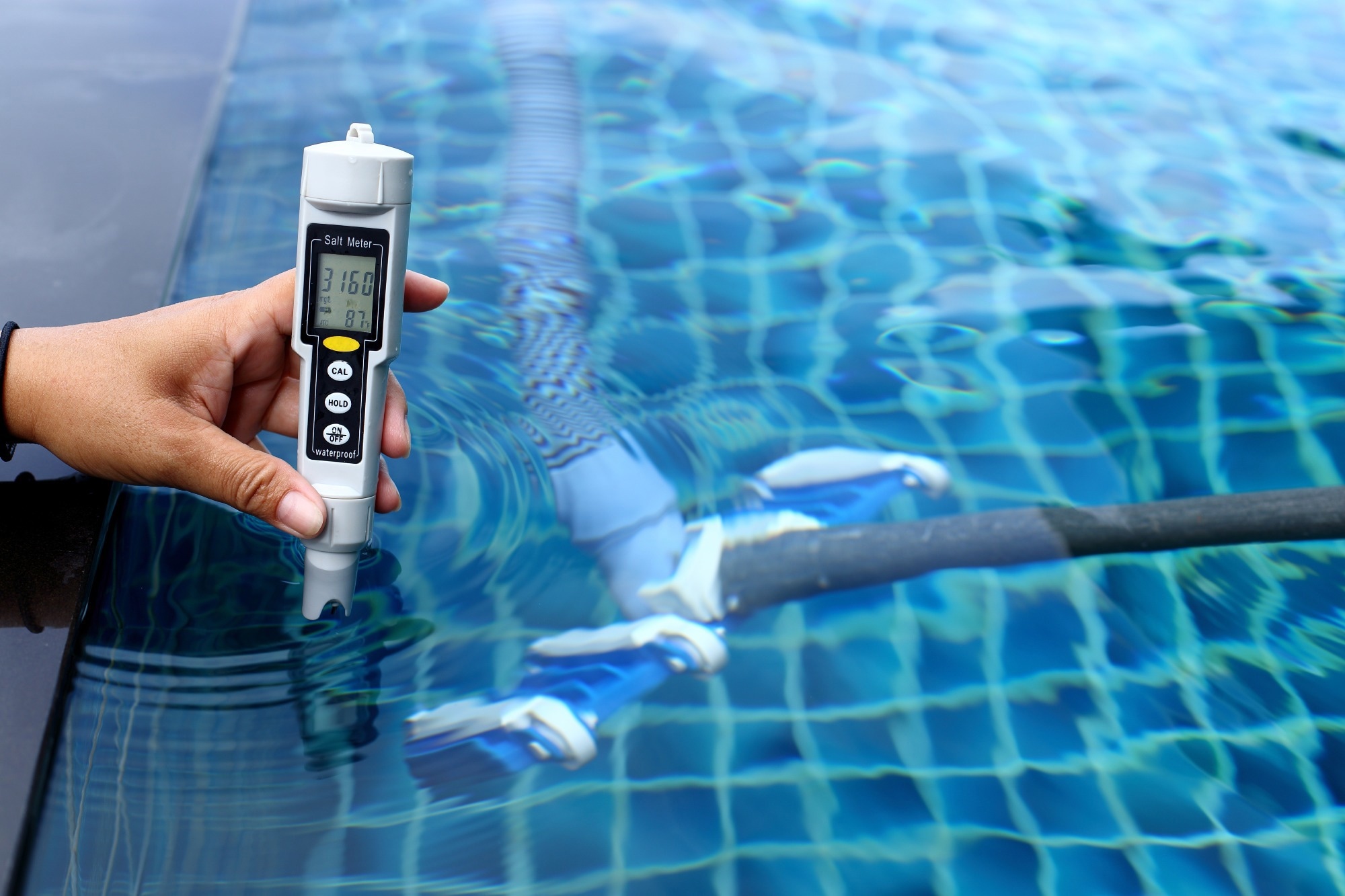 A person using a waterproof salt meter to measure salt concentration in a swimming pool.