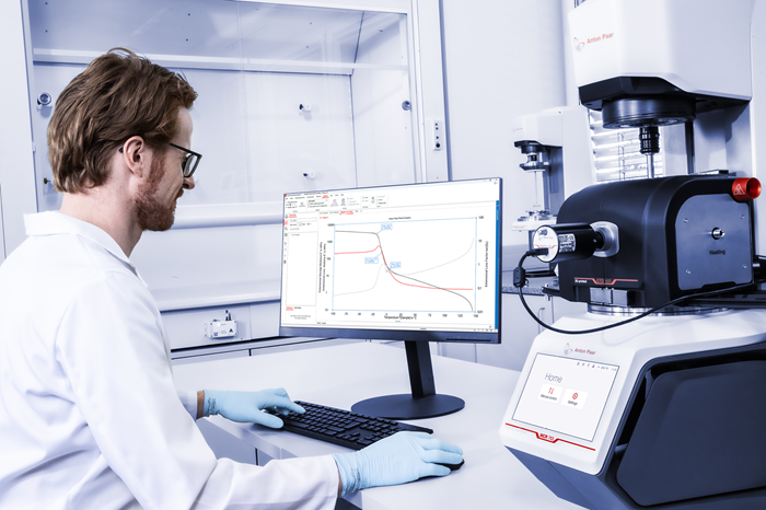A man in PPE uses the MCR 703 MultiDrive for Dynamic Mechanical Analysis and looks at received data.
