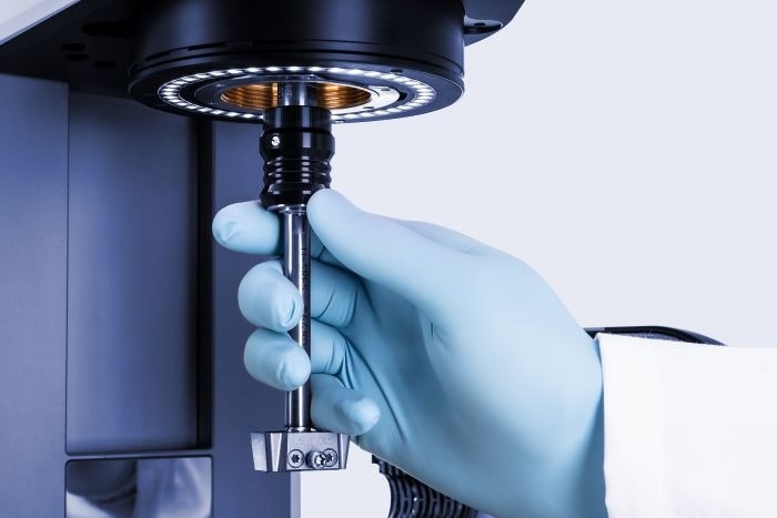 A hand in blue nitrile gloves adjusts the sampling arm of the equipment.