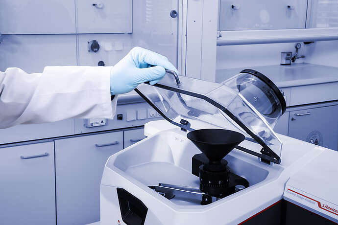 The arm of a scientist wearing a lab coat and blue nitrile gloves opens a compartment of the Litesizer DIA 500
