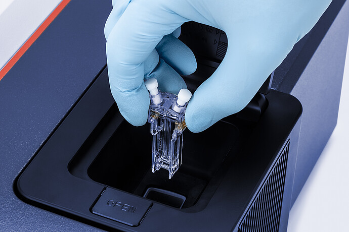 Scientist places cuvette into DLS machine wearing a blue nitrile glove. The sample is colourless.