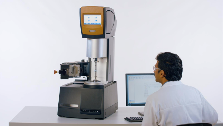 The ARES-G3 Rheometer product image with a man wearing a white lab coat and glasses sitting next to it and examining the instrument.