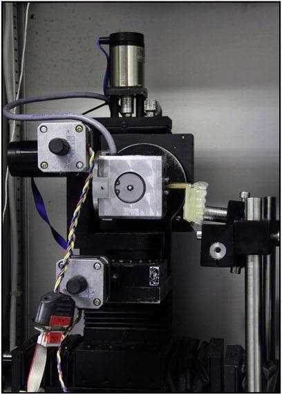 Orthodontic measurement and simulation system (OMSS): a resin replica with a 4D-printed aligner is mounted in the system. Tooth 21 to be analyzed was connected to a computer-controlled 3D sensor. The measured moments and forces are registered, and the motor-driven positioning table simulates the analyzed tooth movement.