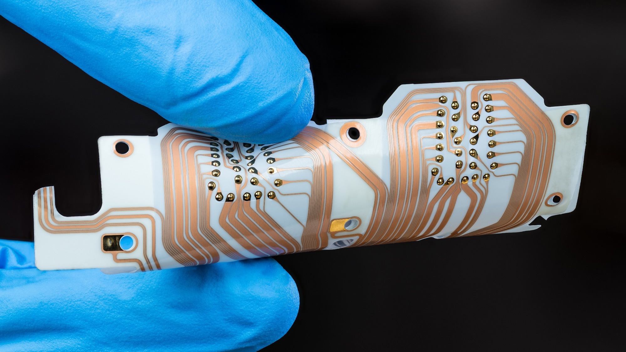 Flex printed circuit board with copper layer in man fingers isolated on black background. Detail of hand in blue glove holding white PCB sheet with integrated connector for computer printer printhead.