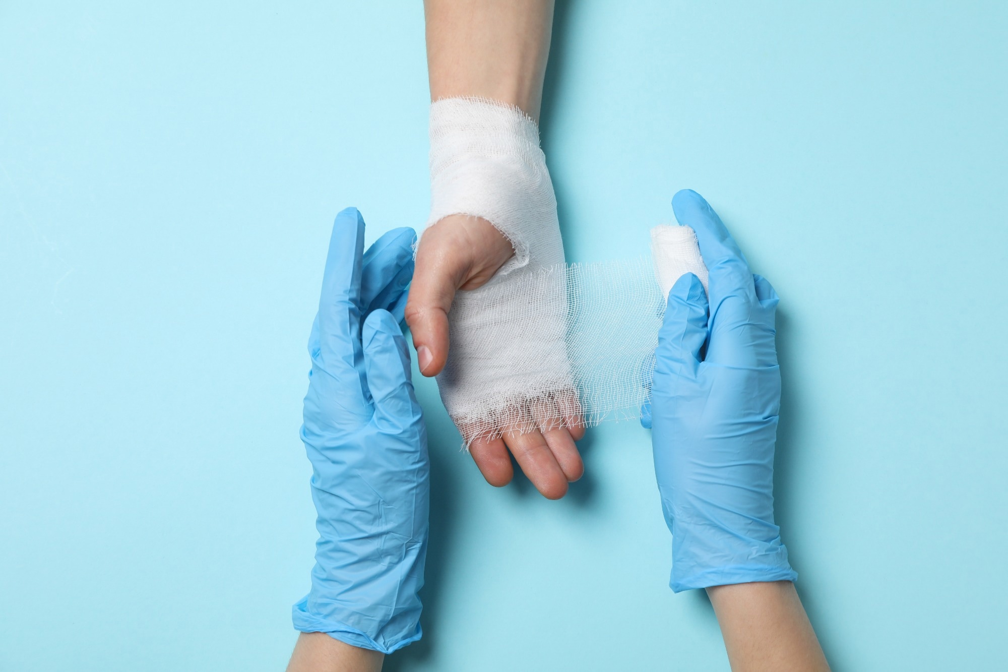 Concept of help during an injury, doctor wrapping hand in bandage on blue background