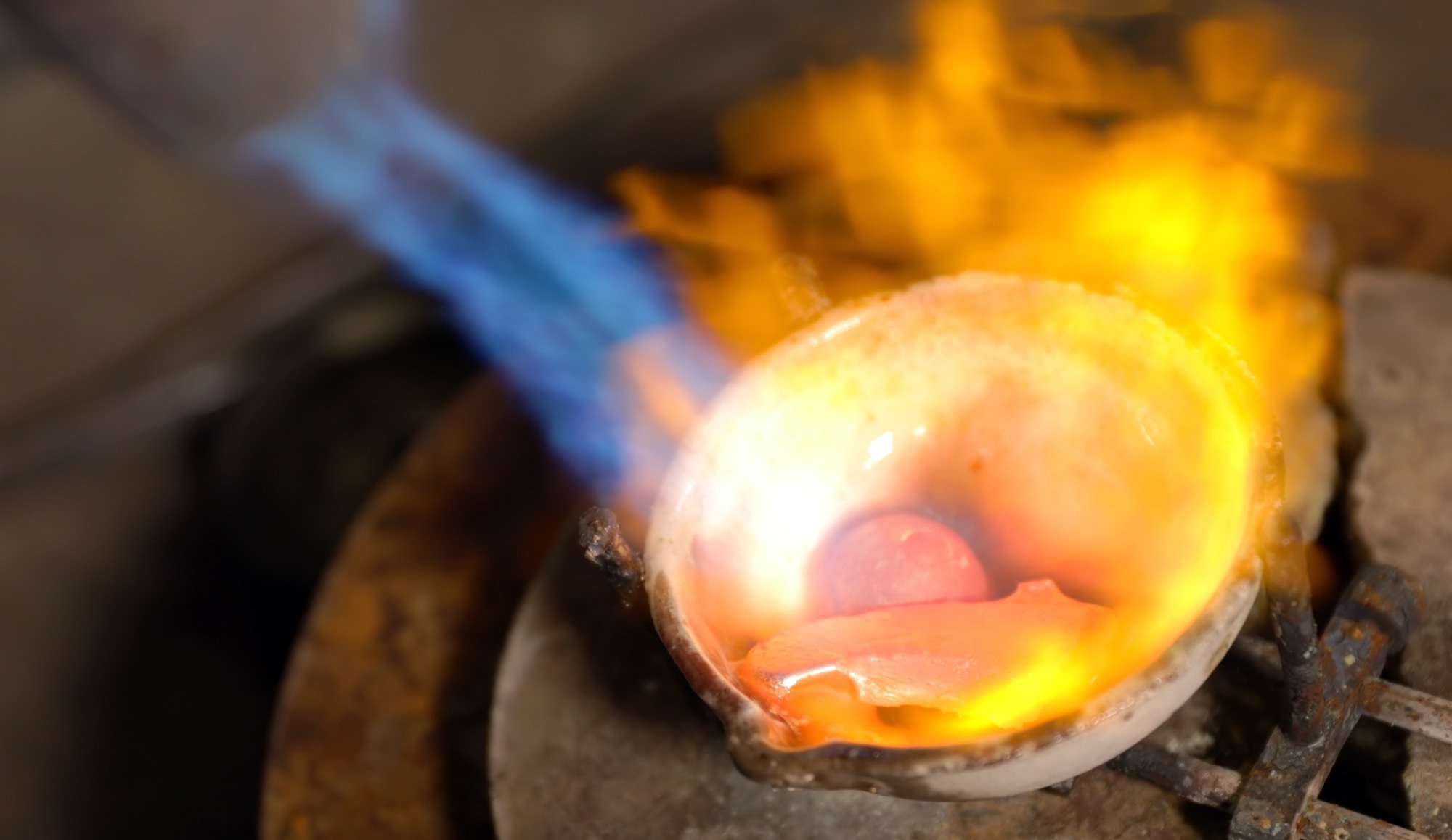 Molten gold being heated further by a blue flame.