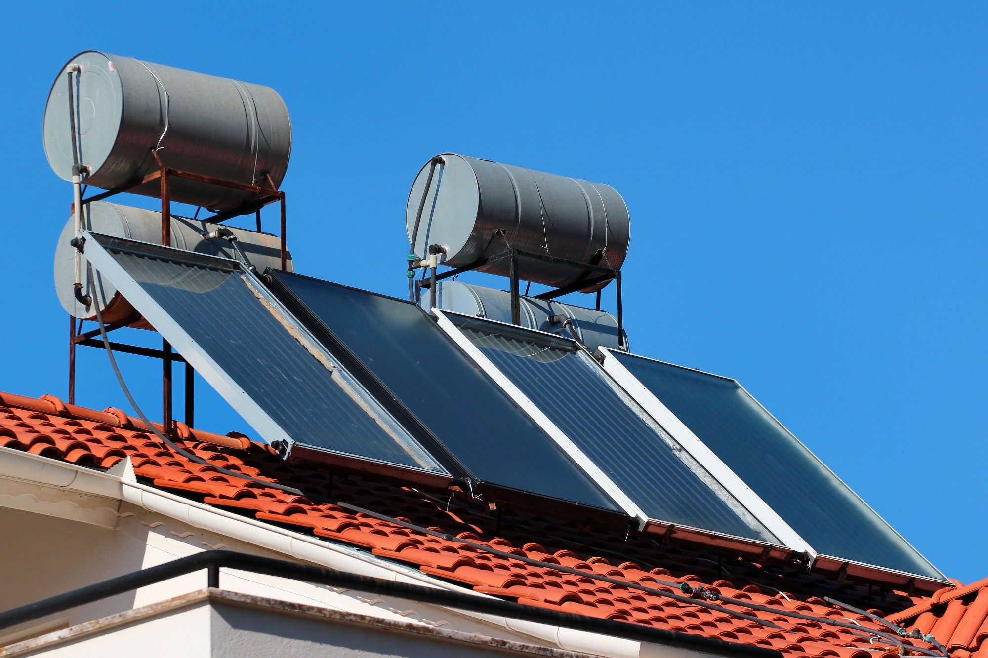 A solar panel water heating cell on top of a roof with a clear blue sky background.