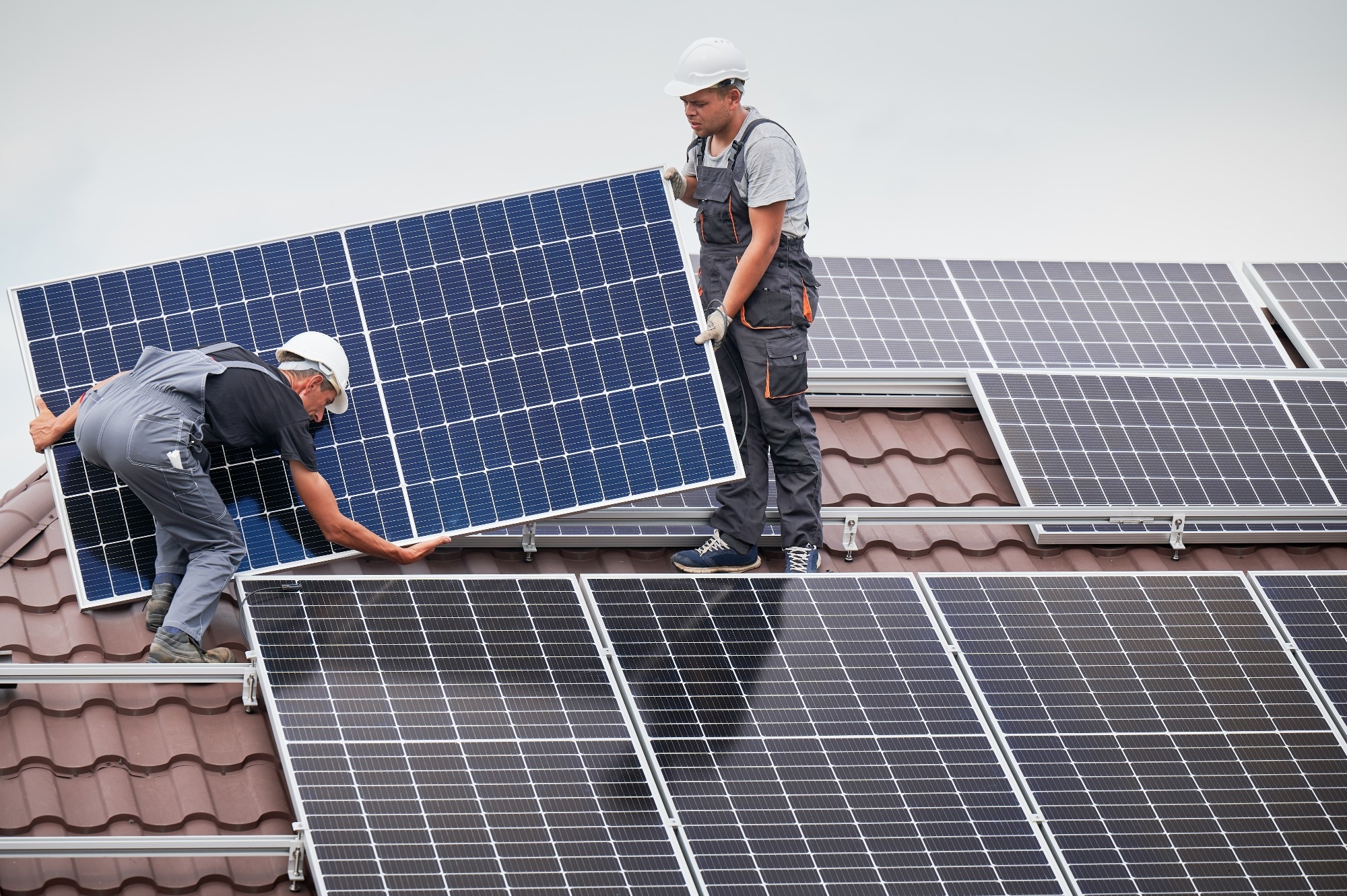 Two men fitting solar cells to a rooftop.